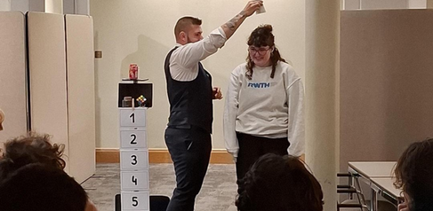 Magiciam performing a trick and pretending to pour water on a volunteers head
