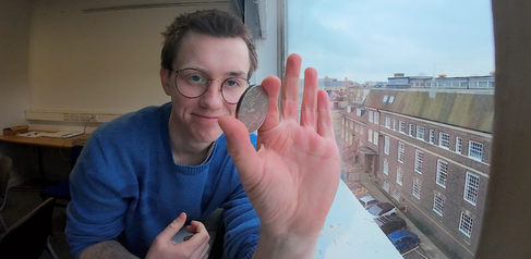 Nathaniel Wright holding a coin, with a university building in the background
