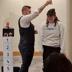 Magiciam performing a trick and pretending to pour water on a volunteers head